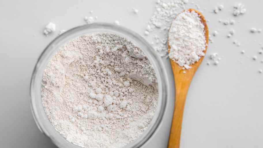 Diatomaceous earth powder in a glass container and a wooden spoon 