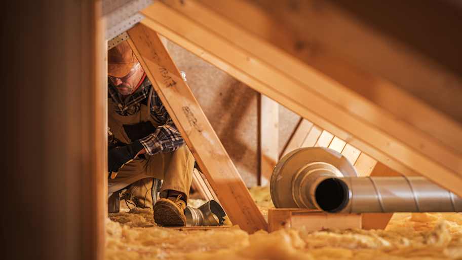 A construction worker is installing insulation in an attic space