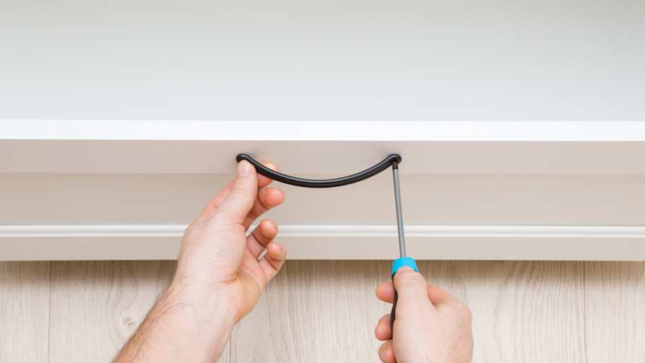 Person using a screwdriver to remove furniture hardware