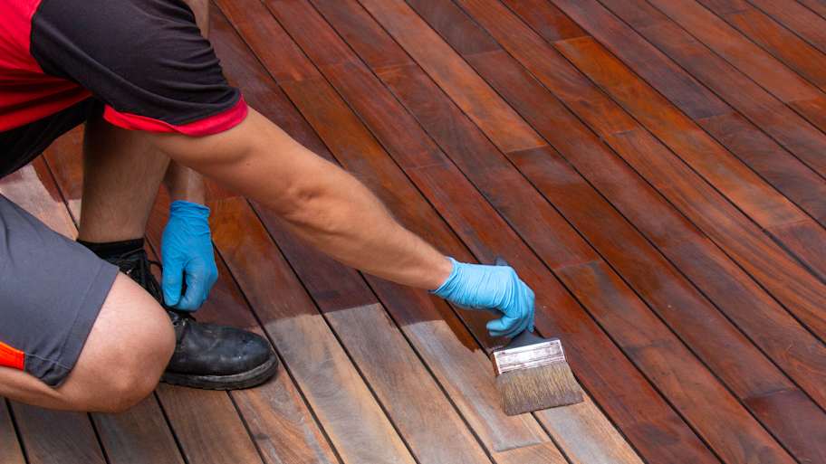 Handyperson using a brush to stain a wooden deck 