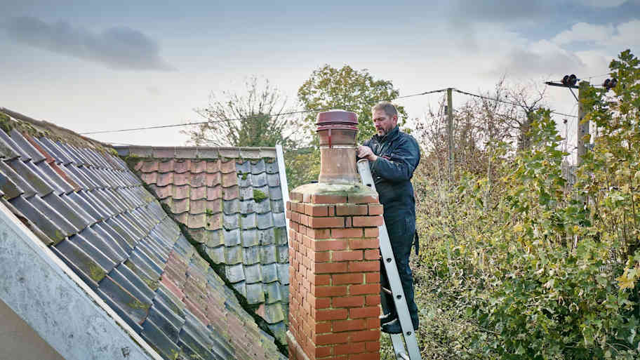 A professional cleaning a chimney while on a ladder