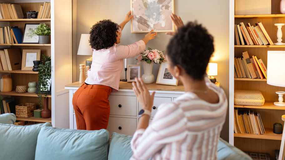 Women lining up picture on wall 