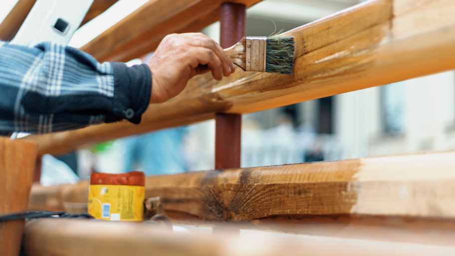 Carpenter varnishing a new wooden fence