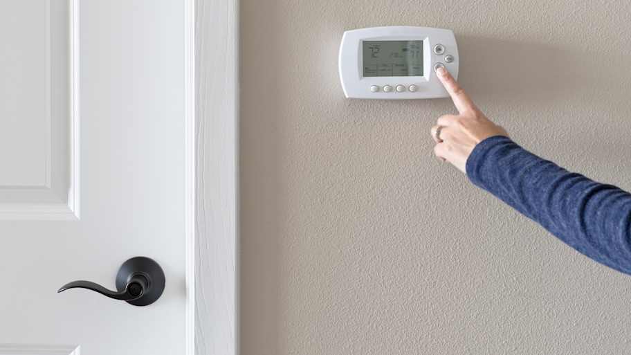 Person using programmable thermostat to turn AC on