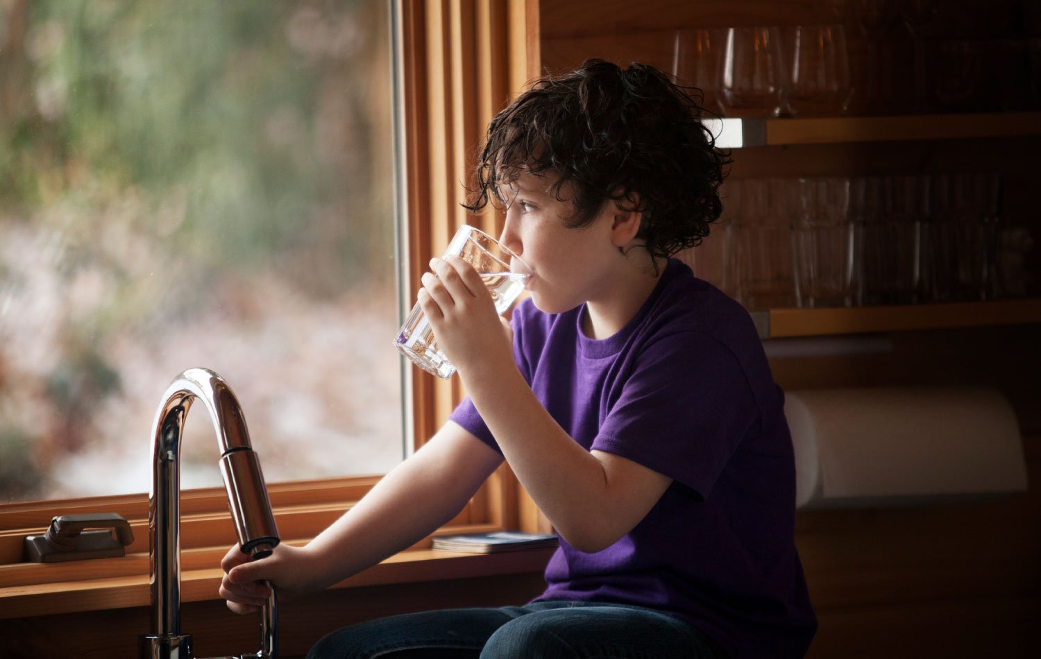 A boy drinking tap water while sitting at kitchen counter