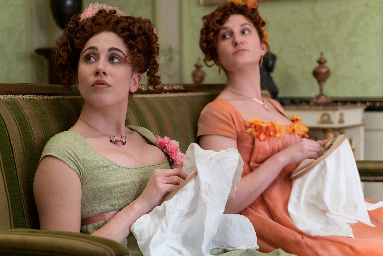 Two Regency era women sitting on a sofa working on sewing projects