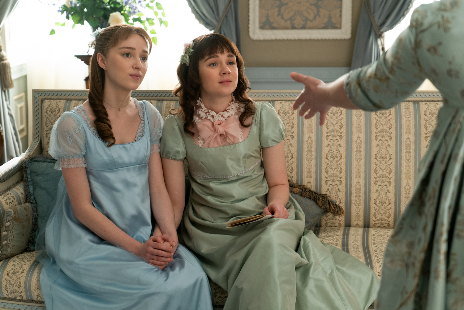 Two Regency era women sitting on a green striped sofa