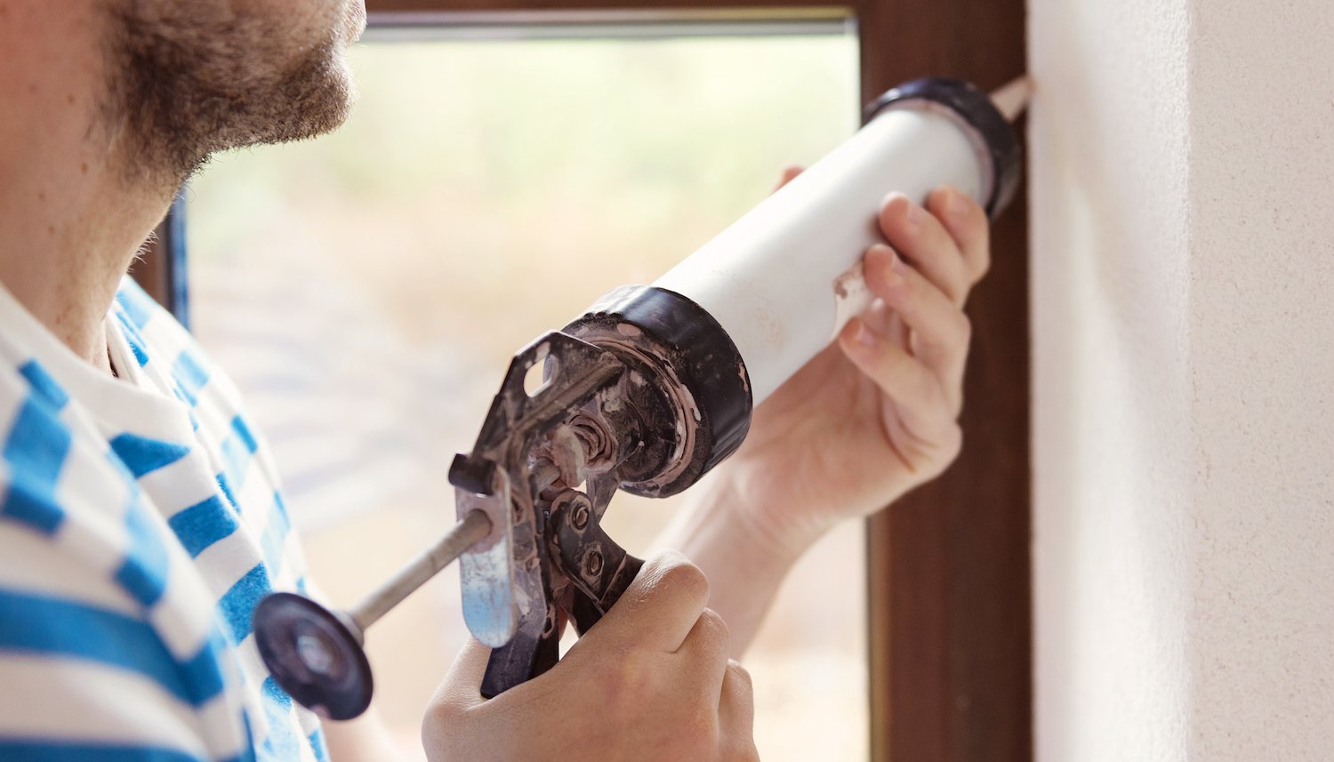 A man applies caulking to a window frame