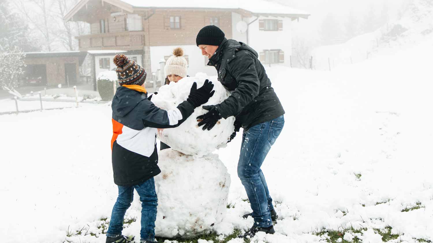 Children making a snowman with their dad