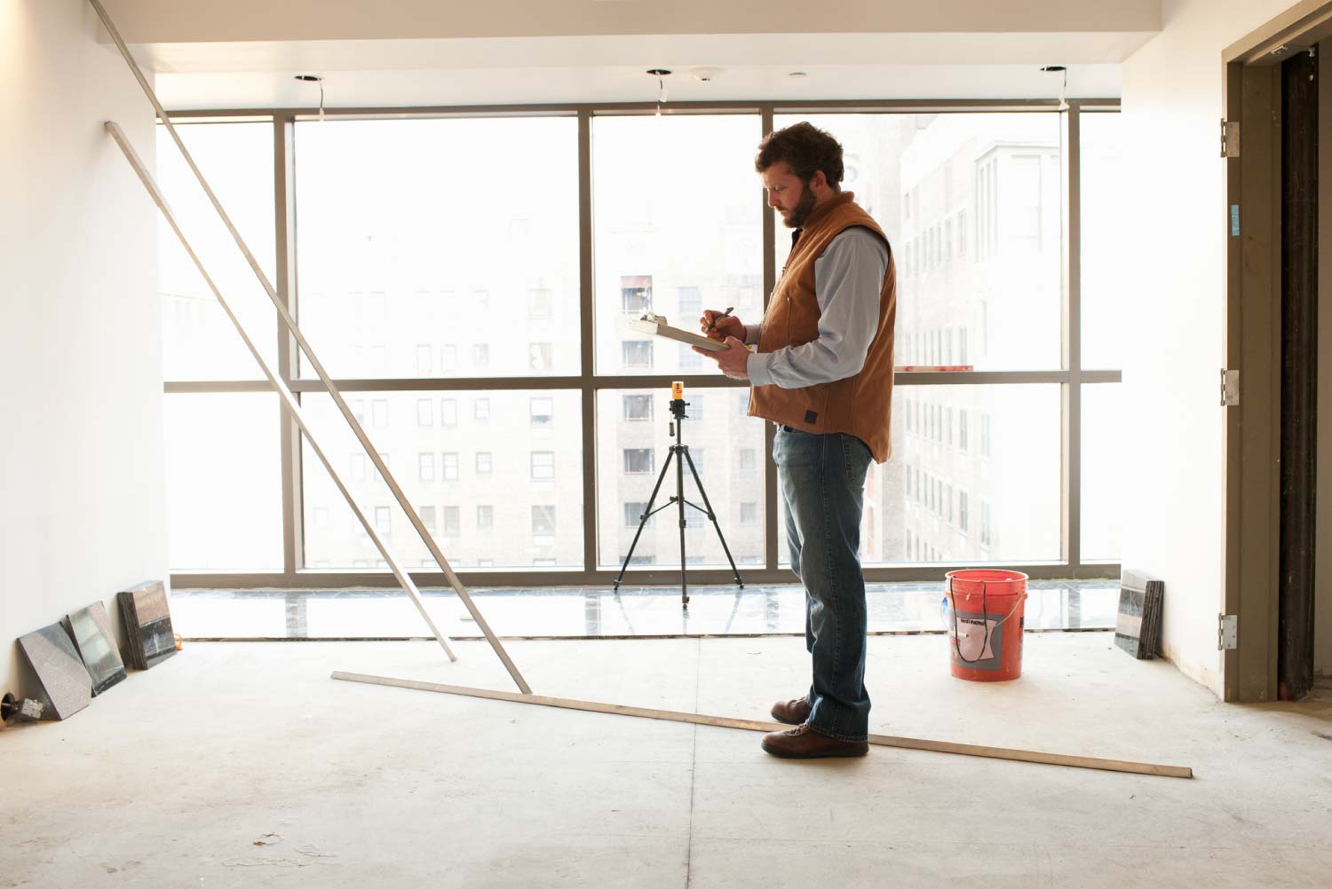 A contractor writing on his clipboard in an empty room at a construction