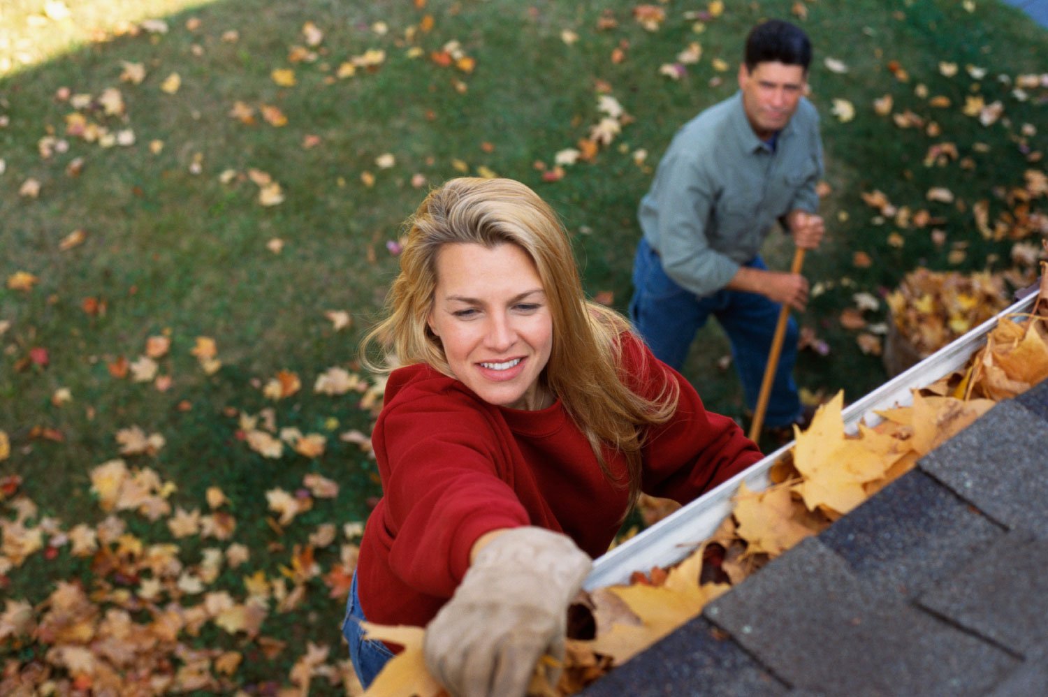 A couple cleaning away leaves from the gutter