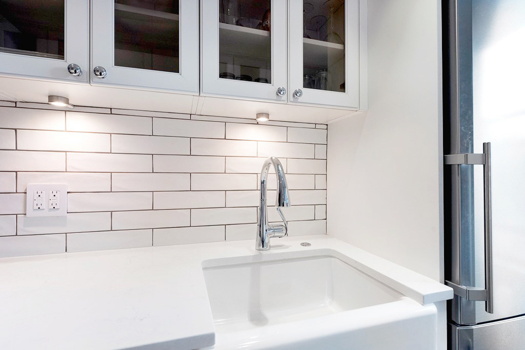 White cabinets and counters with subway tile and apron sink