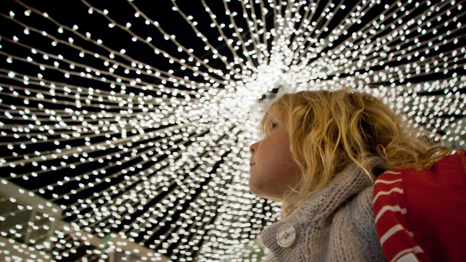 Girl looking upwards at fairy lights