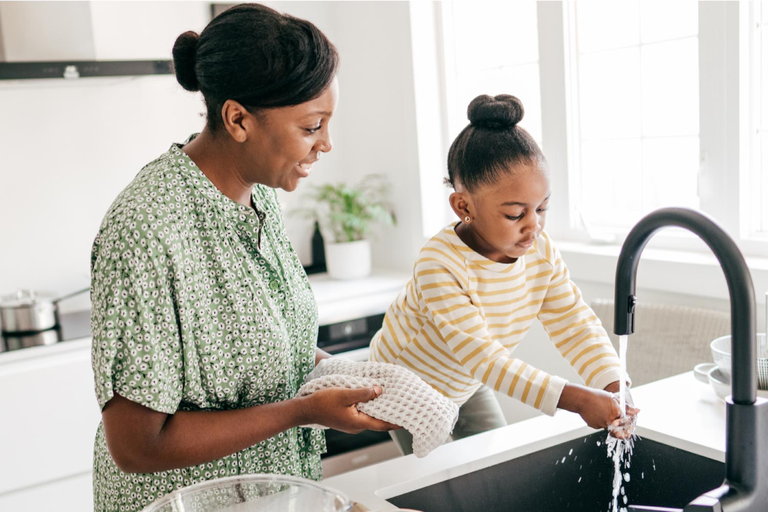 A little girl washing her hands in the kitchen with her mother