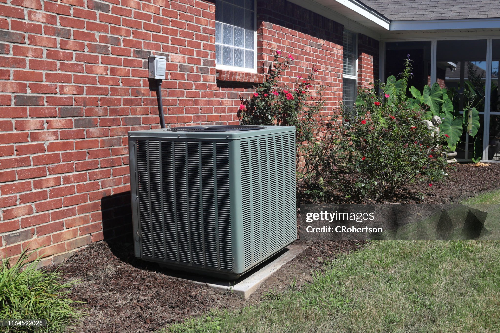 An HVAC system in the backyard of a brick house