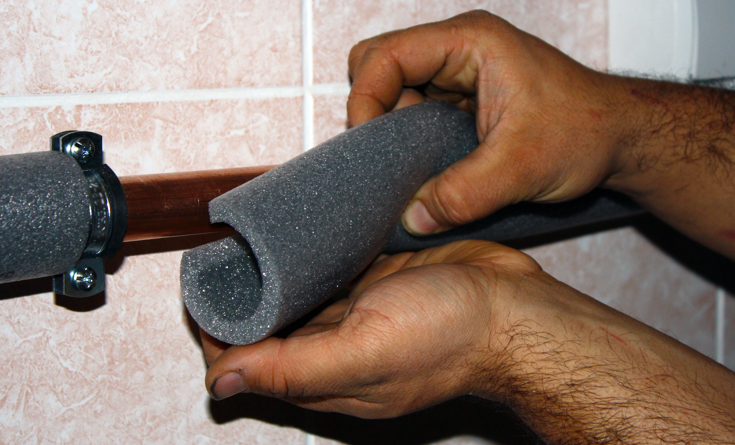 Hands wrapping insulation around a pipe