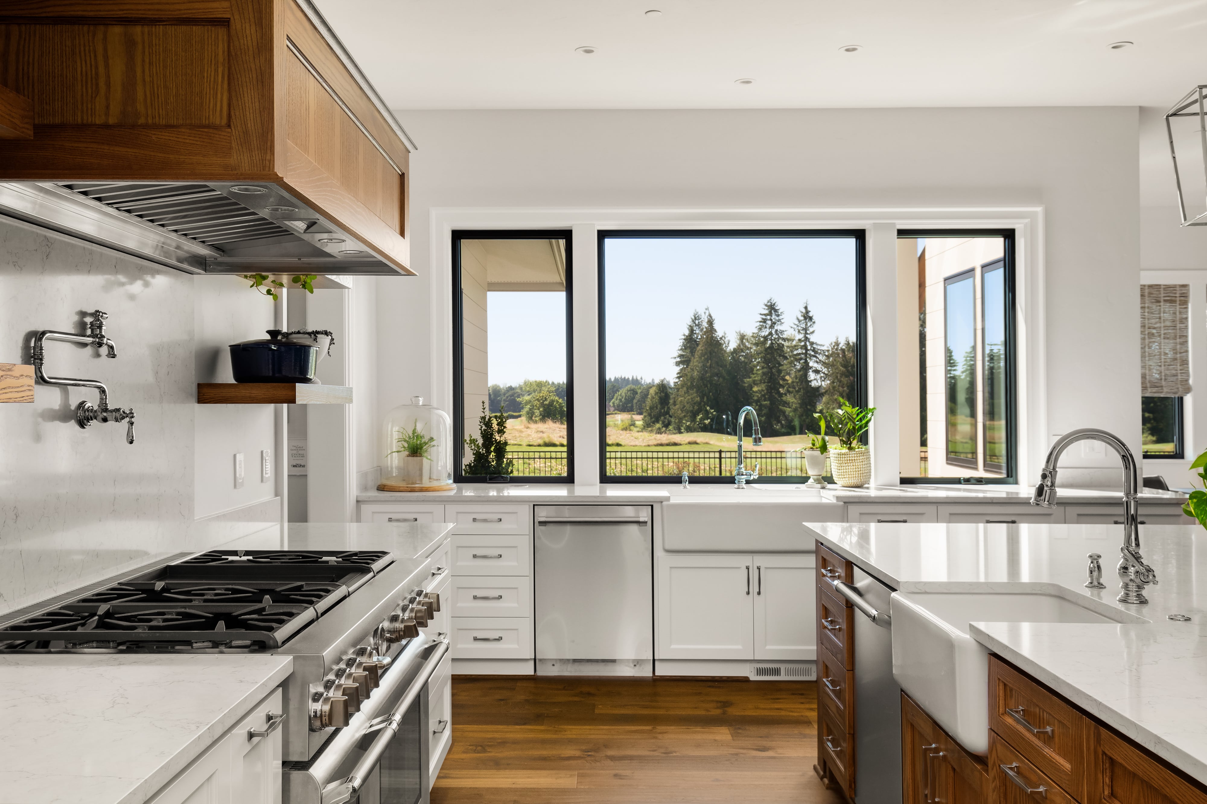 Luxury kitchen with white quartzite counters, two farmhouse sinks, and windows overlooking pine trees