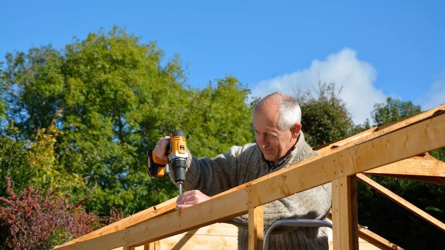 A man using a drill and screws to build a roof frame 