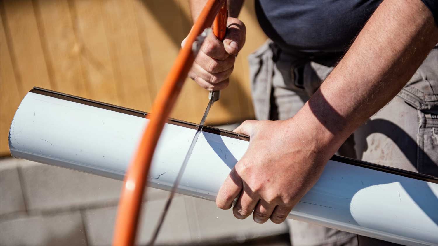 Man cutting roof gutter with hand saw