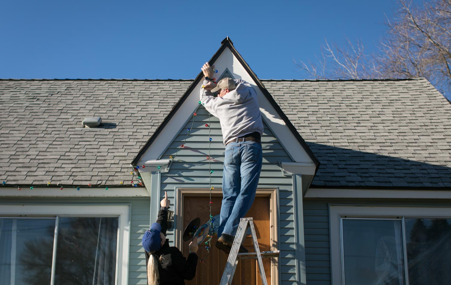A man hanging Christmas lights on peak of a house