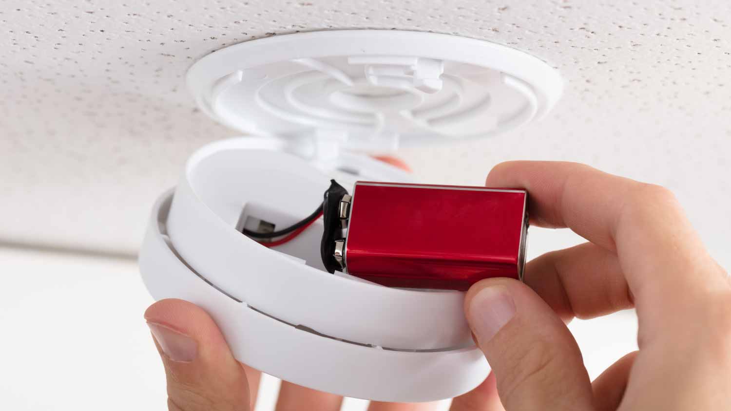 A person installing a battery in a carbon monoxide alarm