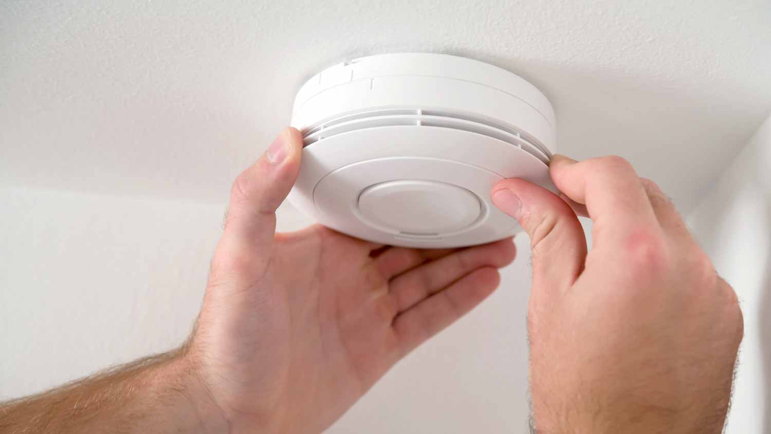 A person installing a carbon monoxide alarm on the ceiling