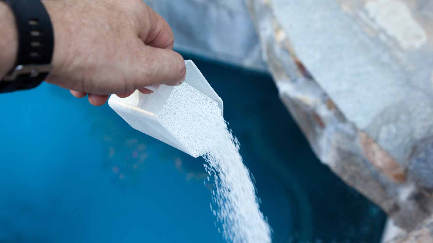 Man pouring liquid chlorine into swimming pool