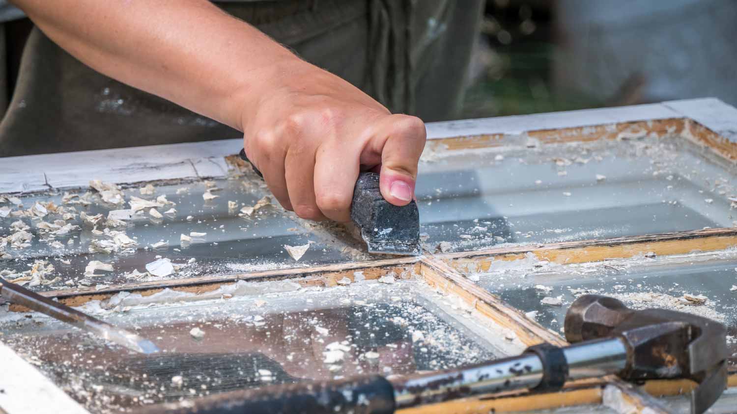 Man scraping old color to fix window