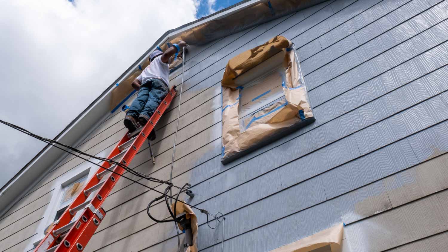 Man spraying paint on the exterior of a house 