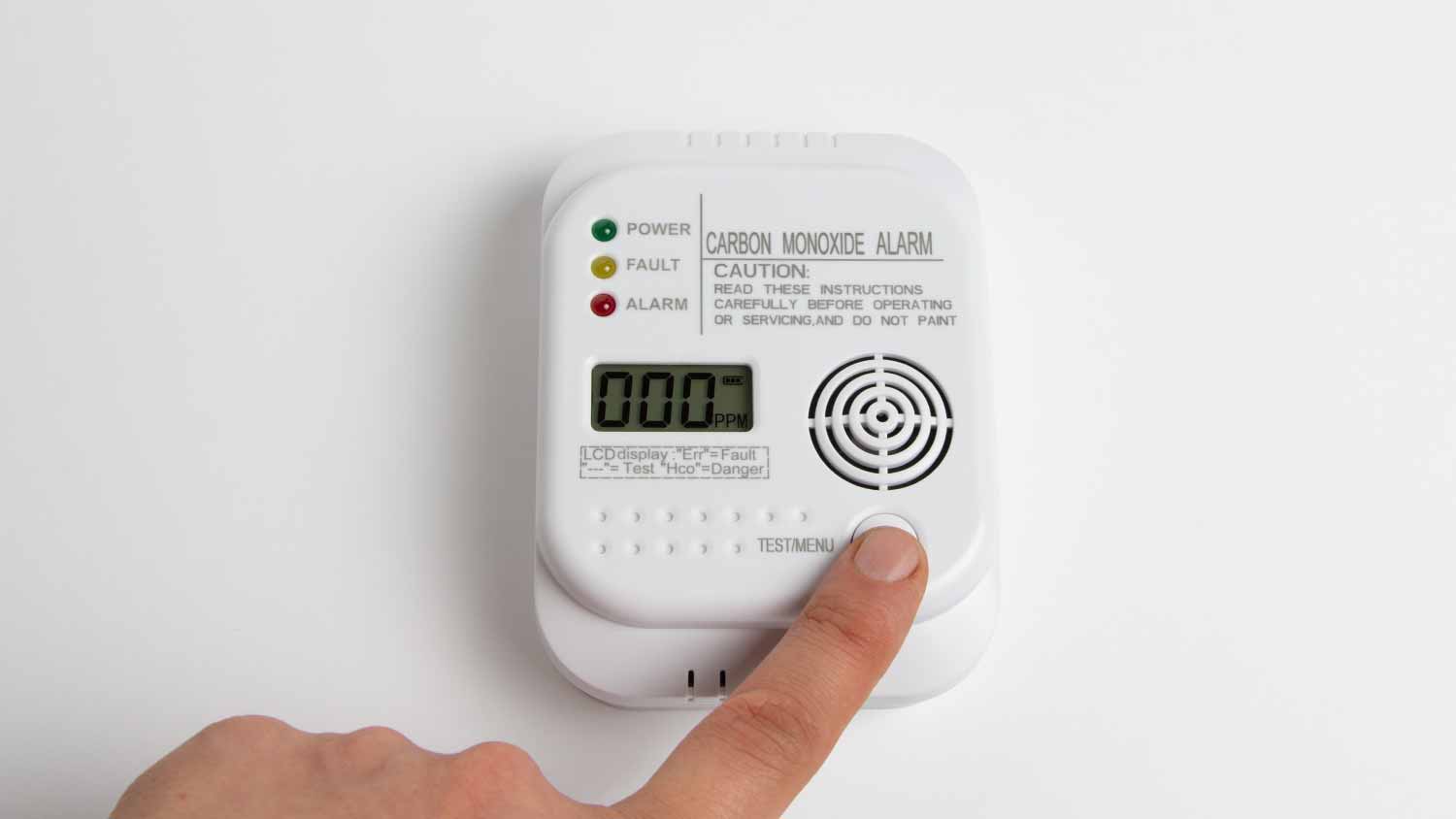 A person pressing the button on a carbon monoxide alarm