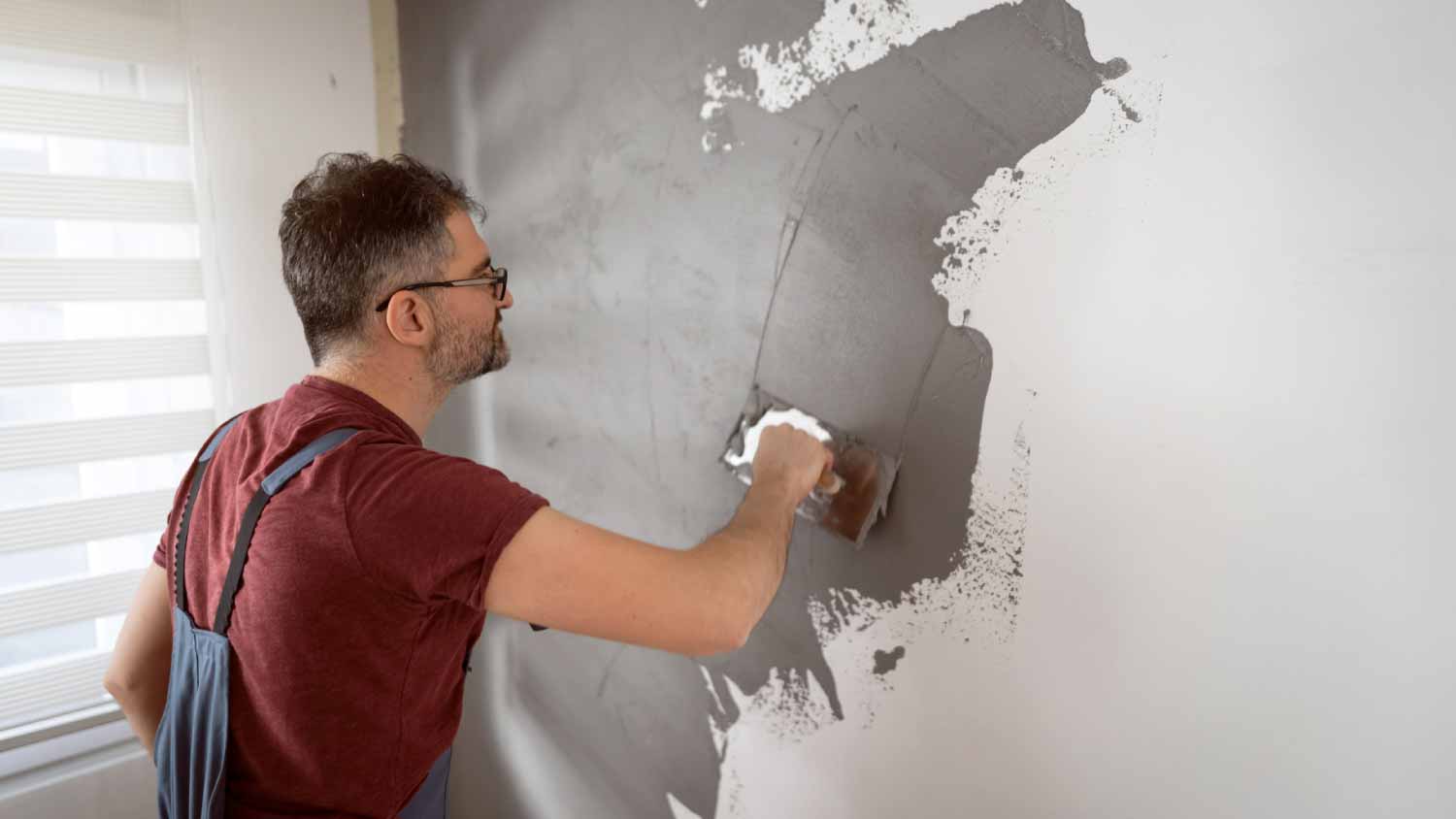 Man using spatula to coat the wall with plaster