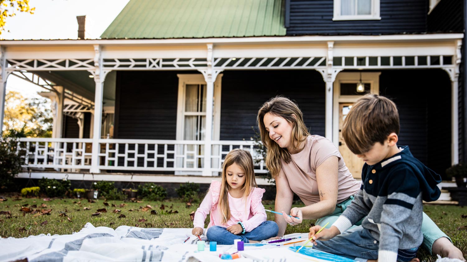 Mother helping children paint in front yard