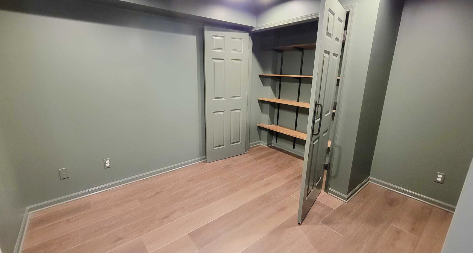 A dark sage green office with a double door closet that has a wooden shelf storage system.