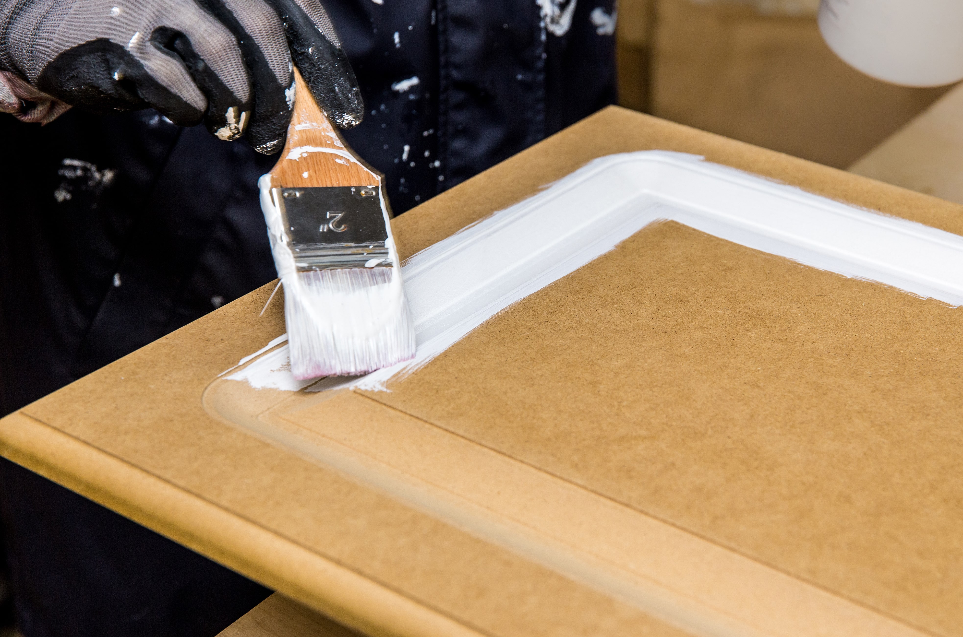 Gloved hand painting kitchen cabinet moulding white with a brush