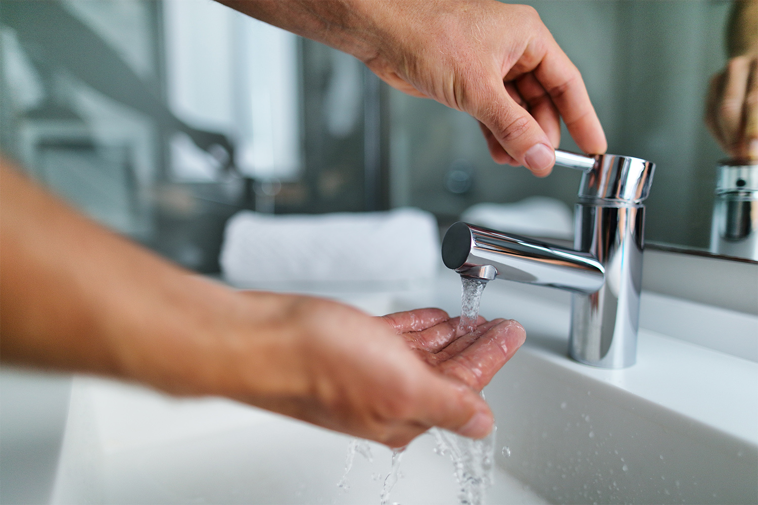 Person testing hot water in bathroom sink