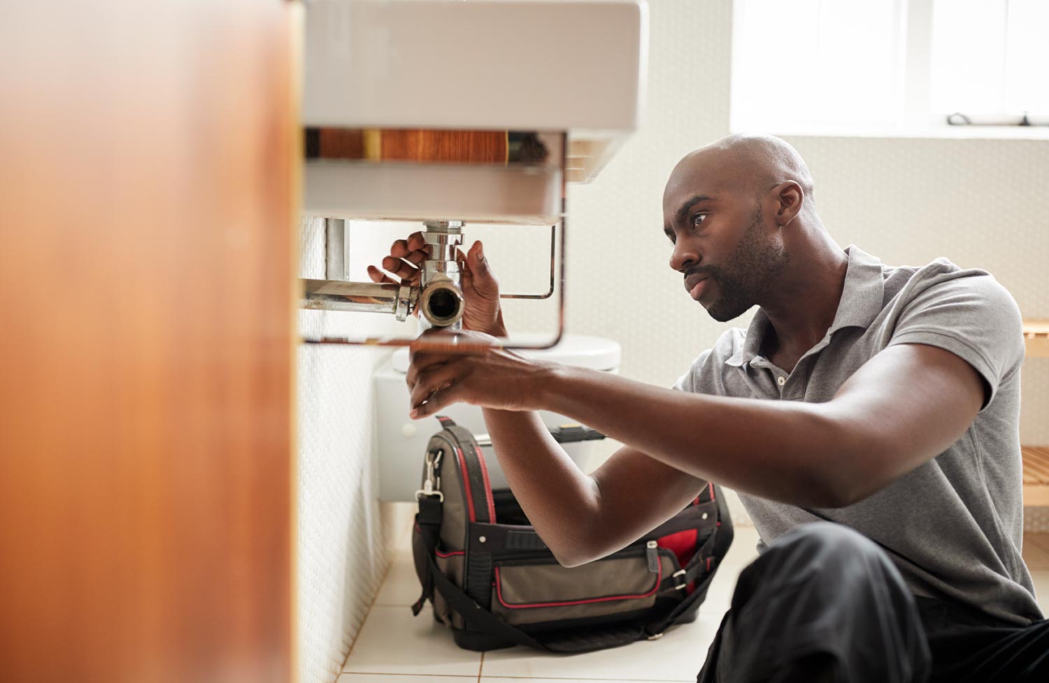 A plumber sitting on the floor fixing a bathroom sink