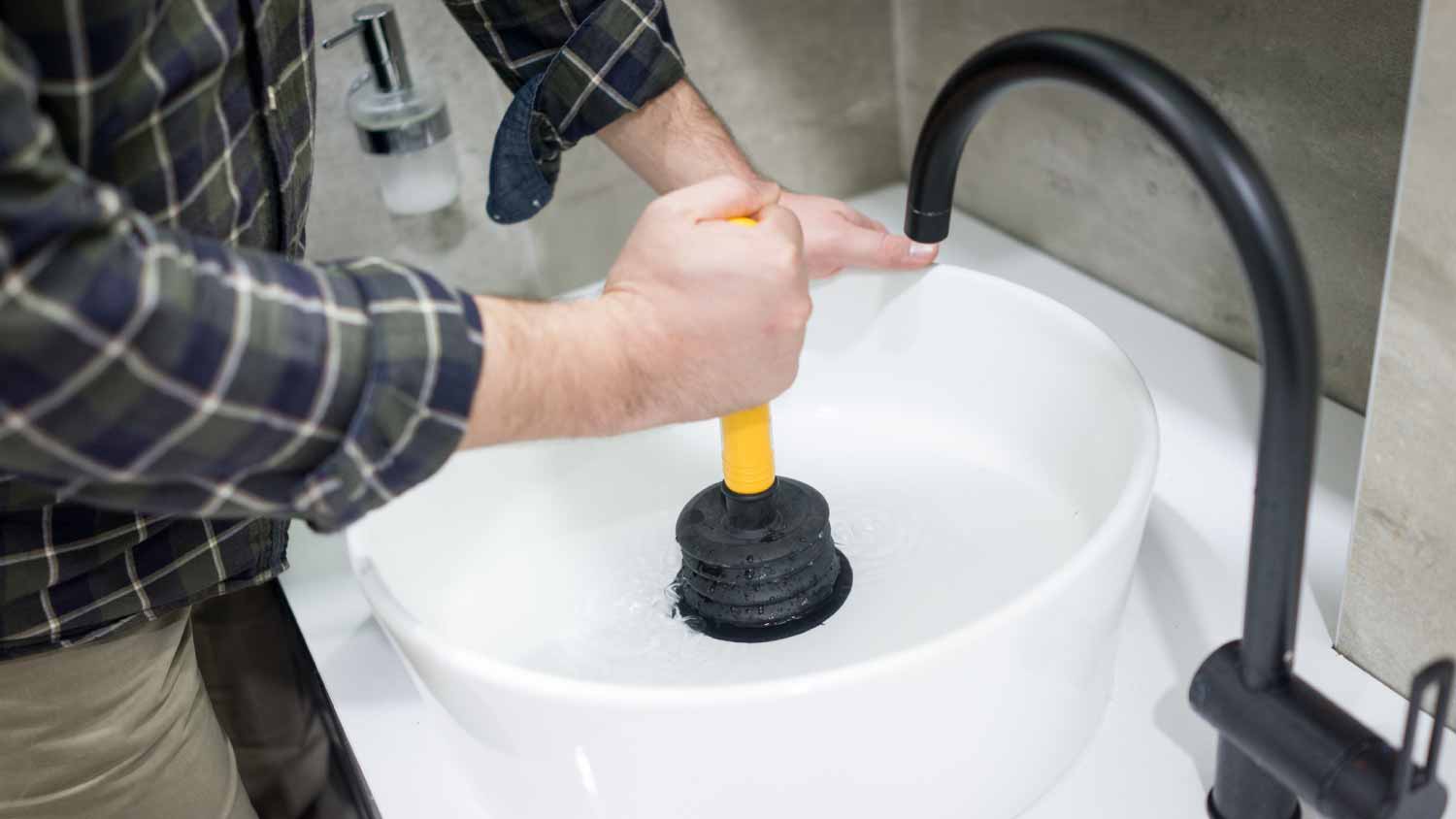 Plumber using plunger in bathroom sink