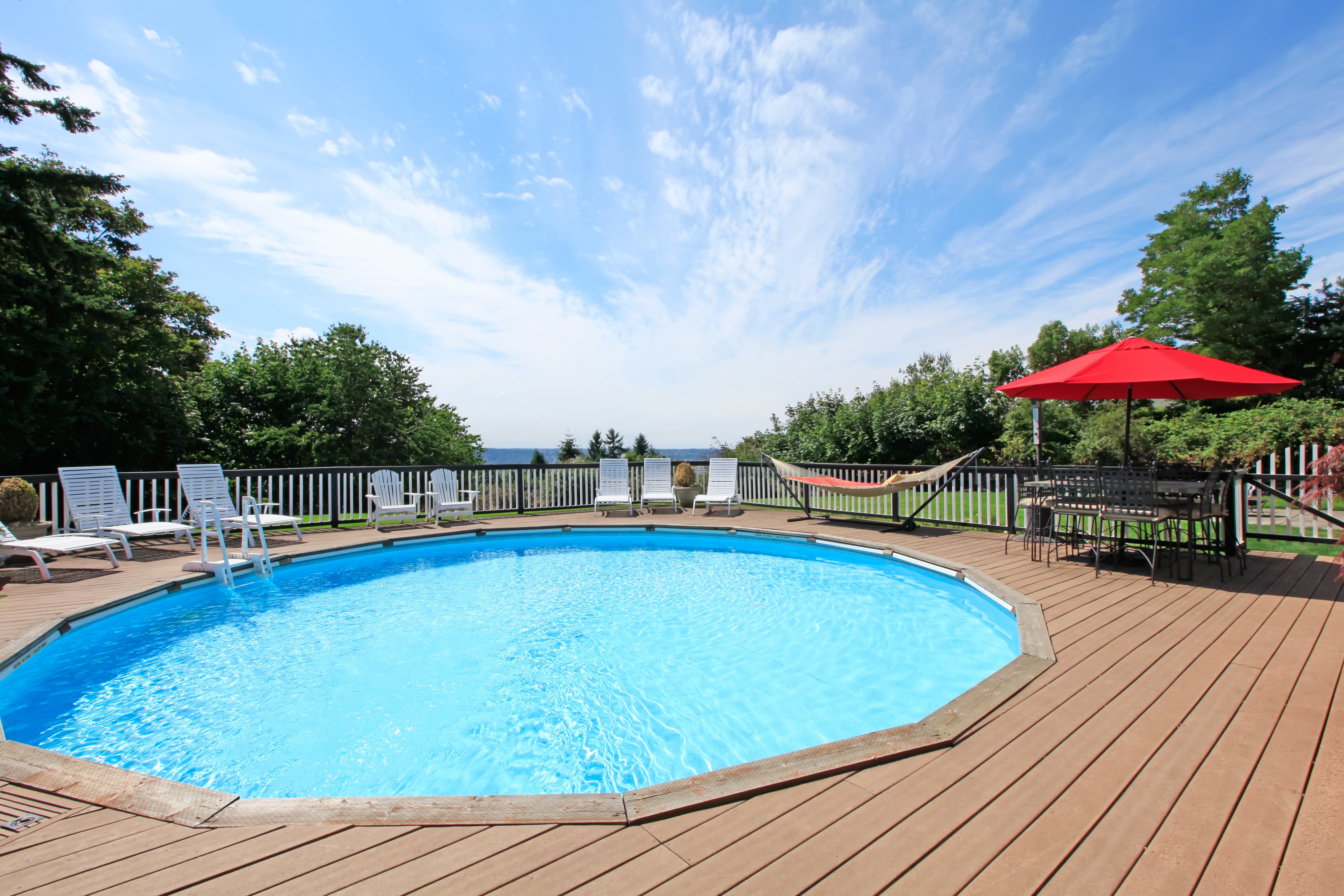 An above ground pool and surrounding deck with lounge chairs, hammock, and patio table