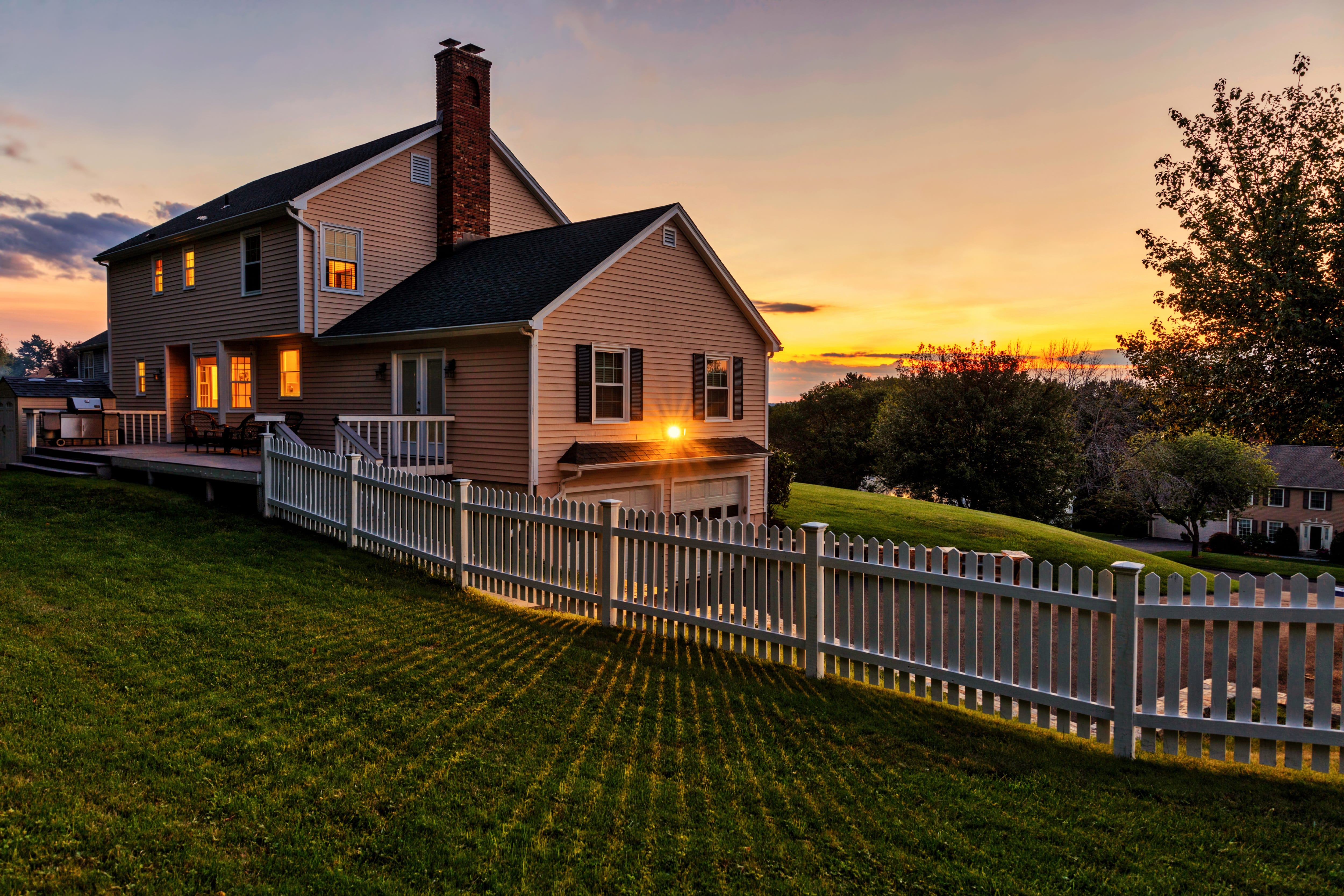 A rural home exterior with a white picket fence