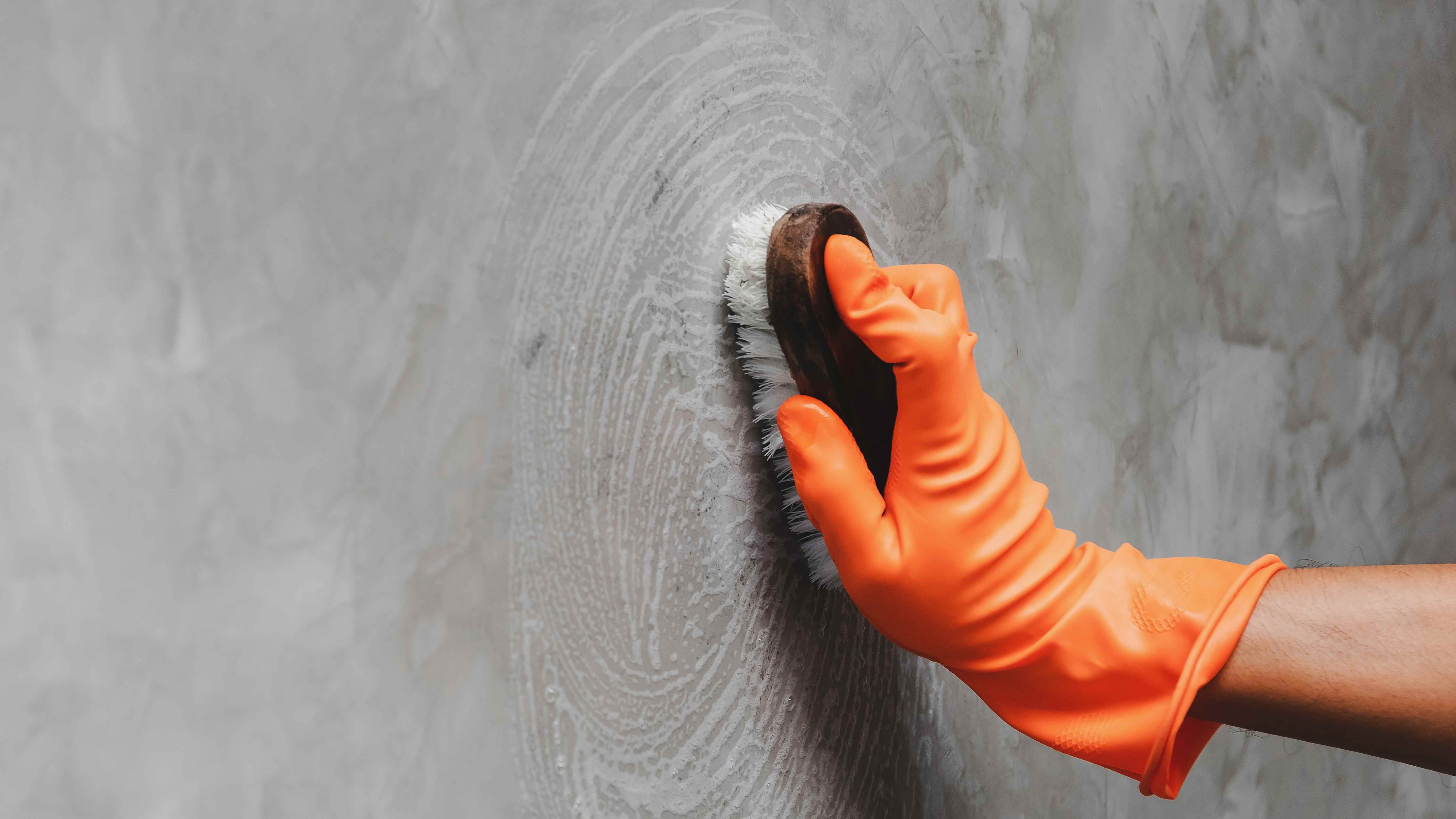 Person in orange glove scrubbing gray wall.