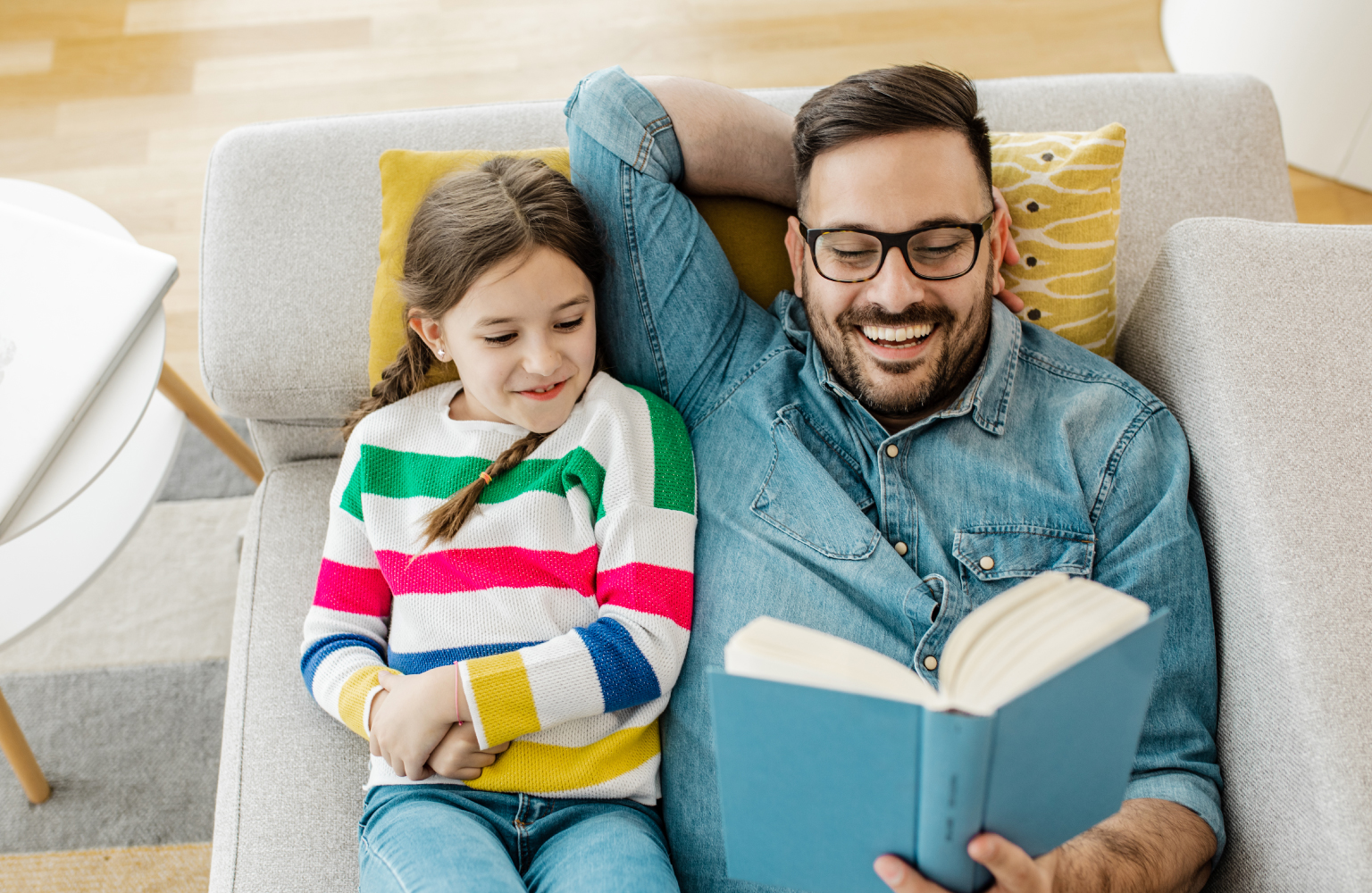 father and daughter reading together on couch 