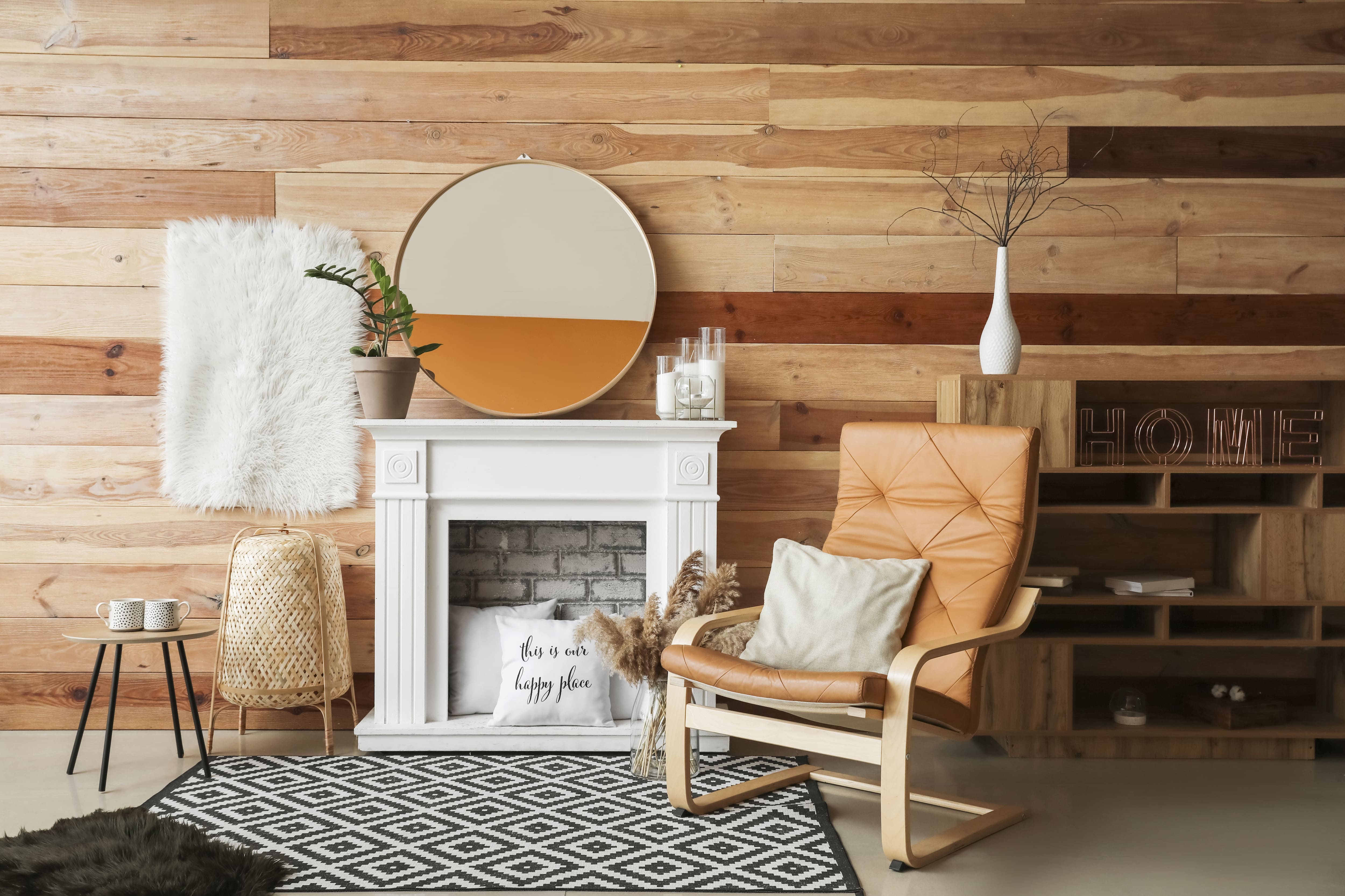 White fireplace, tan leather chair, and wood shelves, and black-and-white rug in front of brown shiplap accent wall