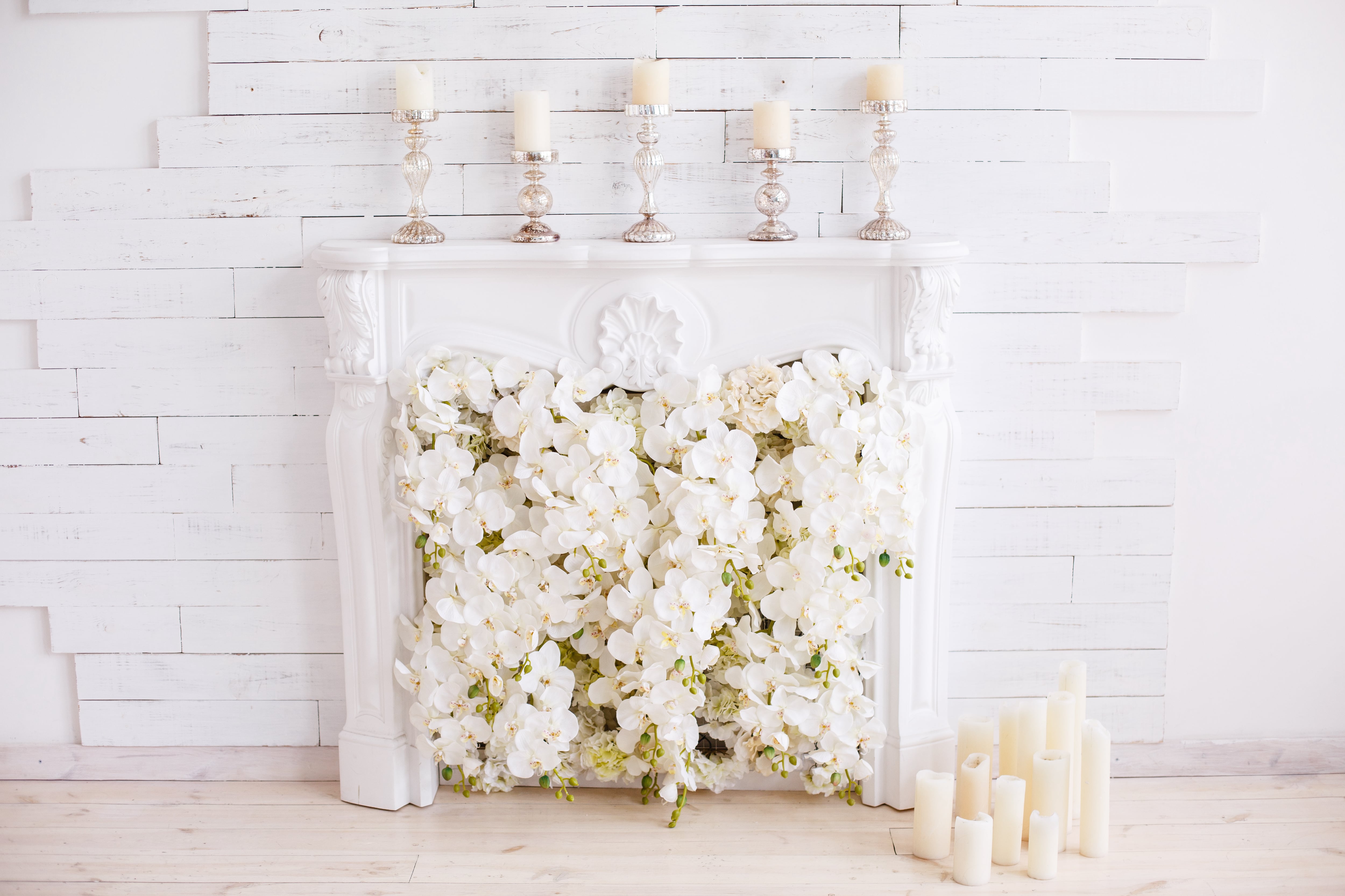 White fireplace with white flowers coming out of it and candles on the mantel against a white staggered-shiplap wall