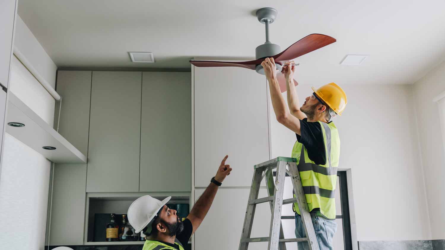 Two technicians installing a wooden ceiling fan.