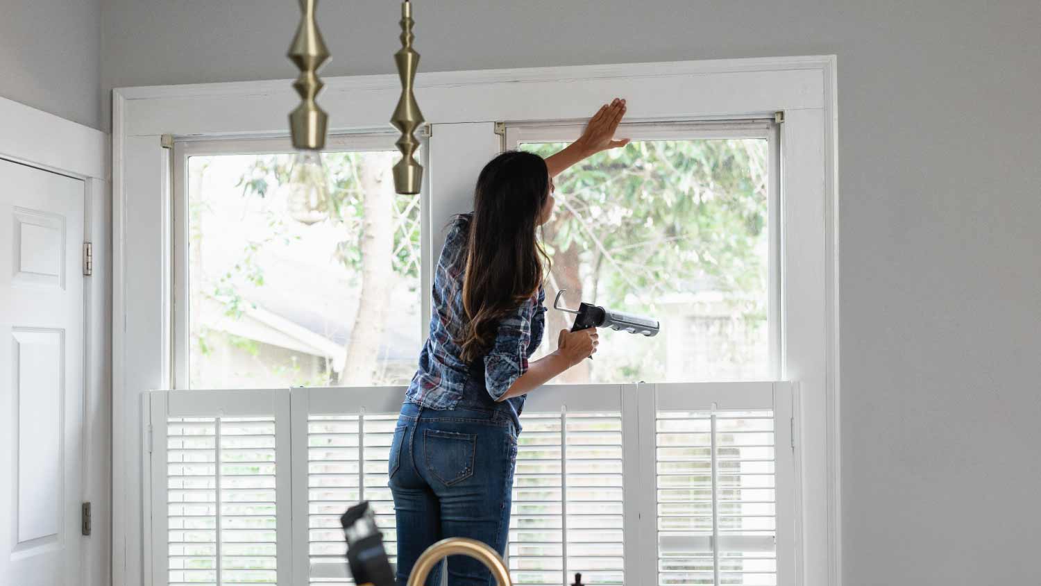 Woman caulking windows for winter