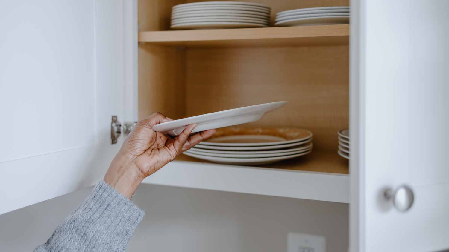 Woman grabbing a plate from kitchen cabinet