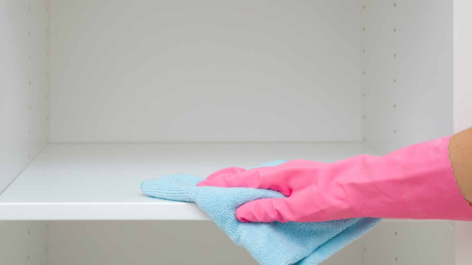 Woman wiping inside wooden cabinets 