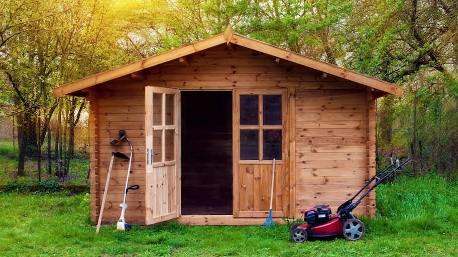 A wooden shed with the front door open and a lawn mower parked in front