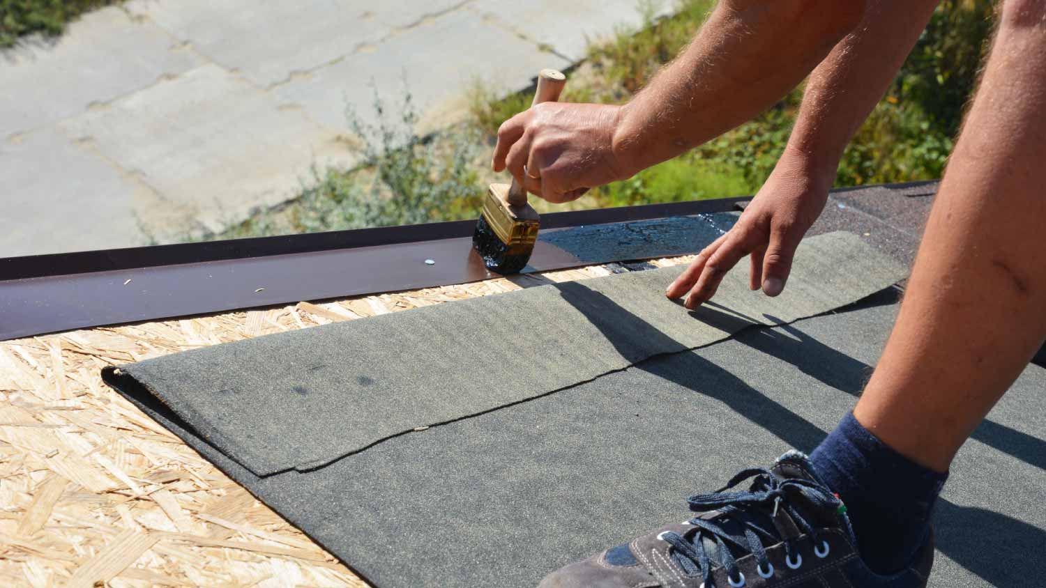 Worker installing layer of bitumen tape