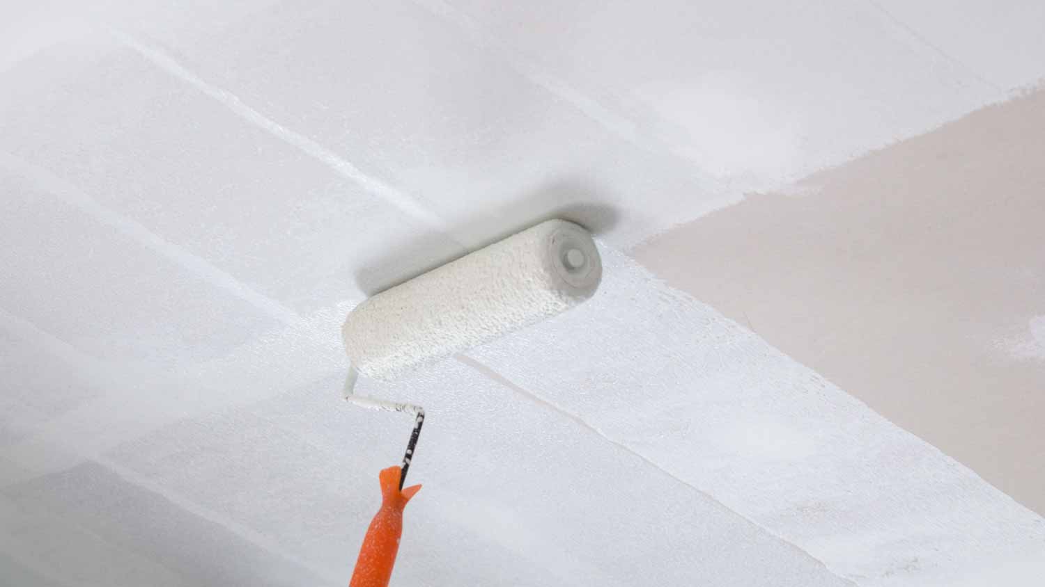 Worker painting a plaster ceiling with roller 